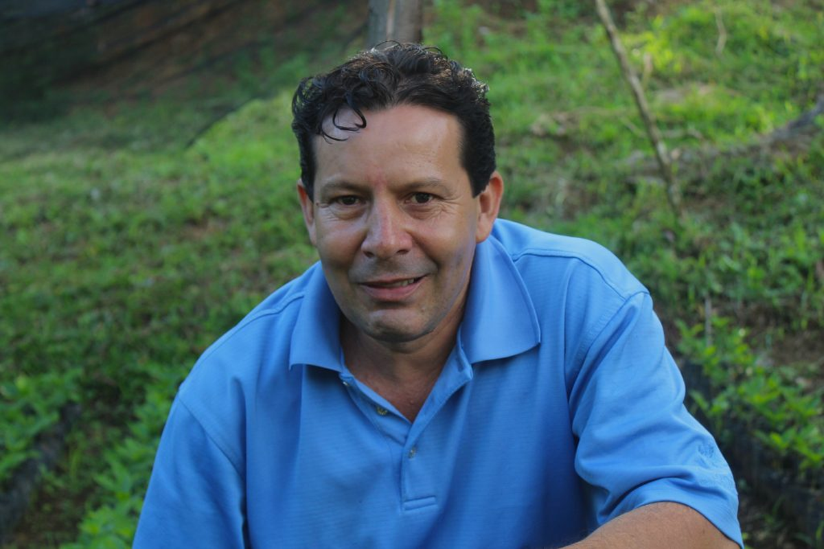 Nelin Guzman wearing a light blue polo shirt, photographed outdoors against a blurred green grassy background.